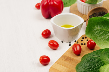 Ingredients for cooking fresh raw spring salad of green and red vegetables, spices, oil with wooden kitchenware on white wood background, border.