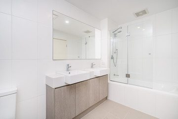 Fototapeta na wymiar Modern minimal bathroom interior with wooden cabinets and glass shower screen.