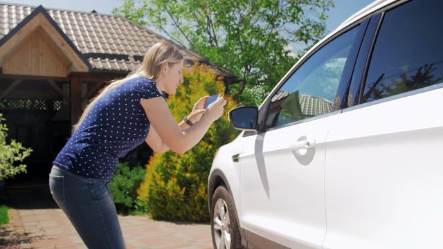 4k footage of young woman making photos of her car on smart phone for selling it