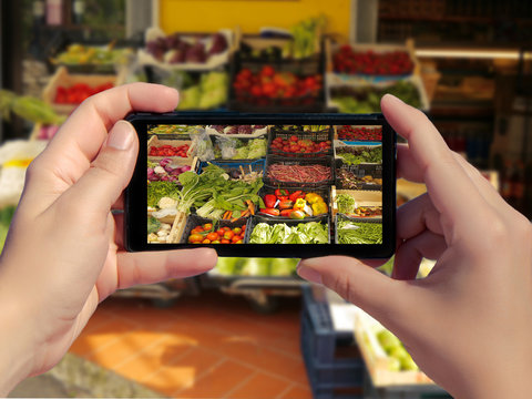 Female taking picture of variety fresh vegetables for sale in a market in Italy on smart phone. Picture of fresh vegetables in the box in mobile phone