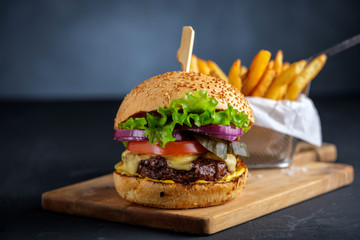 Tasty grilled beef burger with lettuce, cheese and onion served on cutting board on a black wooden table, with copyspace. - obrazy, fototapety, plakaty