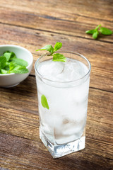 Glass of water with ice and mint on wooden background.