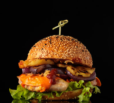Tasty homemade grilled chicken burger with lettuce, cheese, ananas and red onion served on a black table, with copyspace
