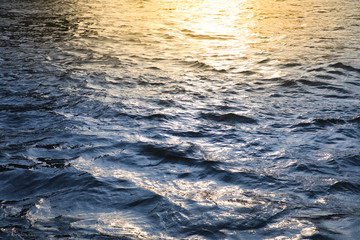 Water surface with ripples and sunrays reflections