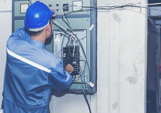 rear view Asian electrician or technician specialist checks or repair or renovation fire panel or connecting wires in distribution board or low-voltage cabinet equipment in Indoor electricity.