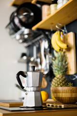 Aluminum gray geyser coffee maker on a stove in the kitchen of a rustic and loft style house, on a chalkboard background and kitchen utensils.