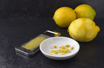 organic lemon fruit, freshly grated peel or rind and the metal grater on a dark slate background with copy space
