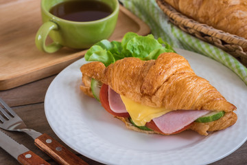 Croissant with ham, cheese on white plate and coffee cup