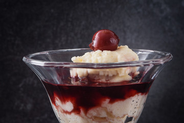 dessert glass with semolina pudding, cherries and fruit sauce on a dark slate background, close up with copy space