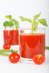 Glass of tomato juice with cherry tomatoes and celery leaves on white background, vertical