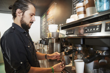Male Barista Using Coffee Machine Behind Counter In Cafe