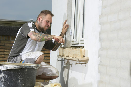 Bricklayer and his bricklayer&acute;s assistant working at a house