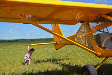Light private plane parked on the grassy airfield and a small child