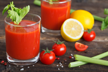 Glasses of tomato juice with cherry tomatoes, lemon and celery leaves on wooden table close up