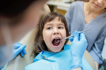 Pediatric dentist examining a little girl teeth in the dentists chair at the clinic