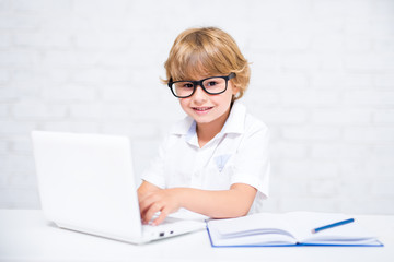happy cute little school boy in glasses doing homework and using laptop