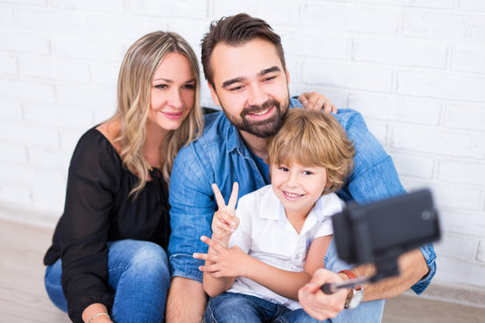 young parents and little son taking photo with smart phone on selfie stick