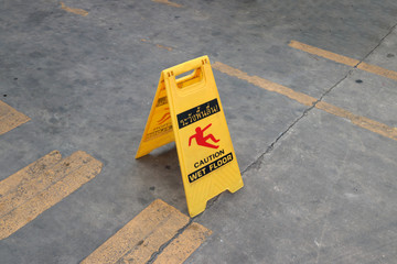 Yellow plastic sign with red symbol of slip and black text of caution wet floor on the floor. the sign of care taken to avoid danger or mistakes.