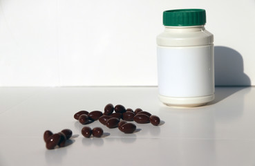 Pile of dark brown medicine on the white floor and white plastic bottle with green cap.