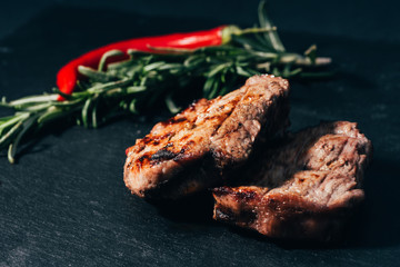 close-up view of gourmet grilled steaks with rosemary and chili pepper on black