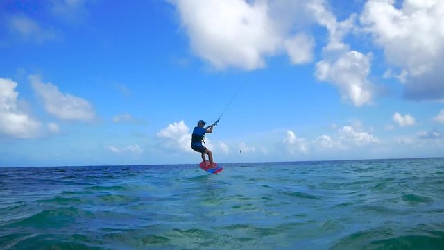 Wide angle shot of kitesurfer riding a foil flying over water in tropical island