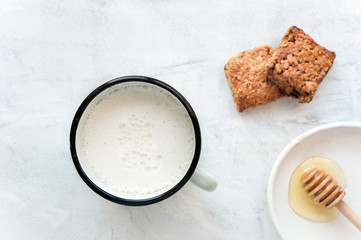Hot milk in a cup and honey on a concrete table. Treatment of hot drink. Cereal cookies. Selective focus. 