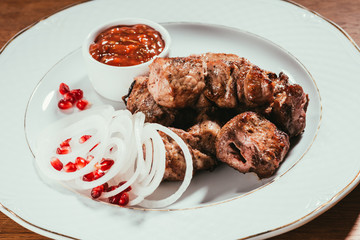 pork slices laying on plate with sauce and sliced onion rings with pomegranate seeds