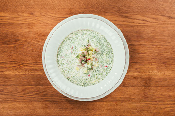 okroshka soup with herbs in white plate over wooden surface