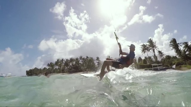 Wide angle shot of kitesurfer riding a surfboard over water in tropical island