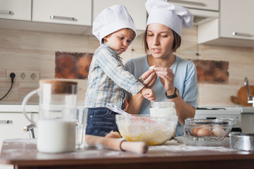 mother teaching her adorable child how to prepare dough at kitchen
