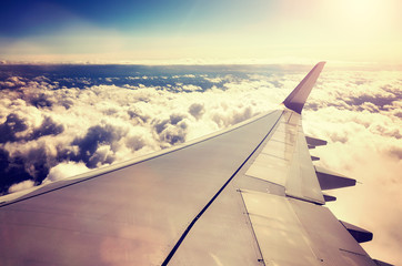 A plane wing above the clouds at sunset seen through a window of an aircraft, color toned travel concept picture.