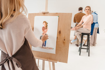 cropped shot of woman painting on easel while model sitting on chair in art studio