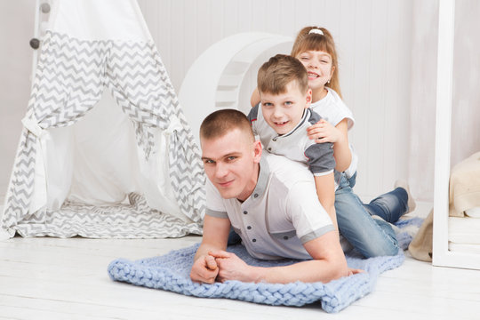 Father with his two little children lying at floor and having fun. Looking at camera.
