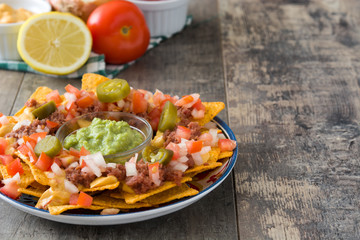 Mexican nachos with beef, guacamole, cheese sauce, peppers, tomato and onion in plate on wooden table