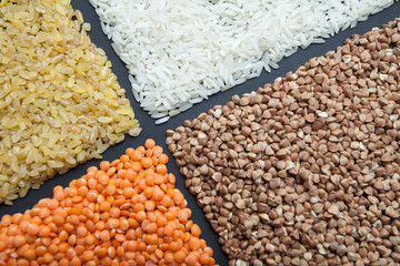 Organic rice, bulgur, buckwheat and lentils on a black background.
