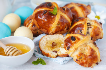 Easter cross buns with honey and butter, painted eggs. Light background, copy space, Easter food concept.