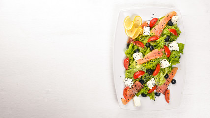 Salmon salad, feta cheese, salad leaves and fresh vegetables on the plate. On a wooden background. Top view. Free space for text.