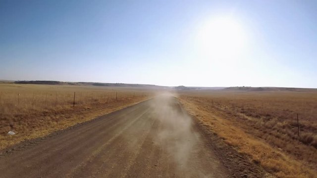 Looking back on dusty road between arid fields with sun just over horizon