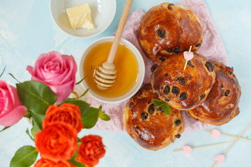 Breakfast for Valentine's Day. Buns with raisins, butter and honey, bouquet of flowers. Top view, blue background. Valentine's Day concept.