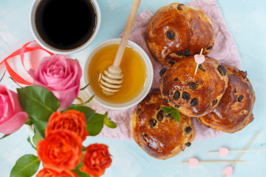 Breakfast for Valentine's Day. Buns with raisins, butter and honey, coffee, bouquet of flowers. Top view, blue background. Valentine's Day concept.