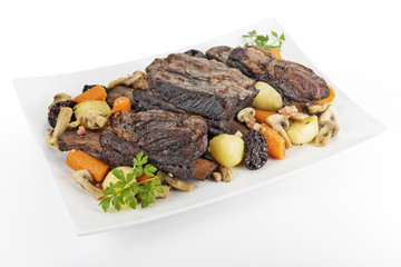 White rectangular plate with three cooked beef ribs mushrooms carrots and potatoes