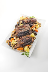White rectangular plate with three cooked beef ribs mushrooms carrots and potatoes