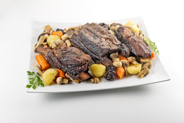 White rectangular plate with three cooked beef ribs mushrooms carrots and potatoes