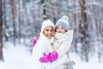 portrait of smiling daughter and mother hugging each other in winter forest