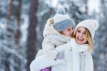 portrait of cheerful mother and little kid piggybacking together in winter park