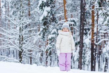Fototapeta na wymiar cheerful kid looking at camera while standing in winter forest