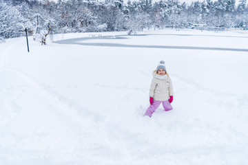 Fototapeta na wymiar adorable happy child standing in snow and smiling at camera in winter park