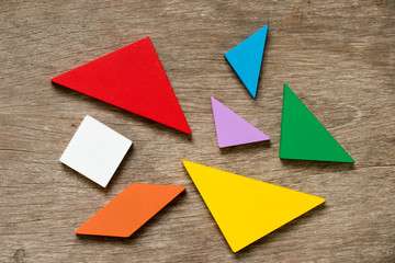 Colorful tangram puzzle wait to develop shape on wood background