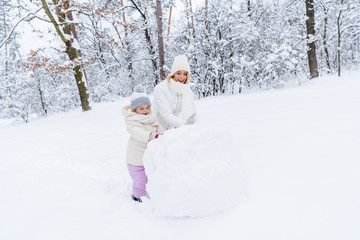 Fototapeta na wymiar beautiful happy mother and daughter making snowman in winter park