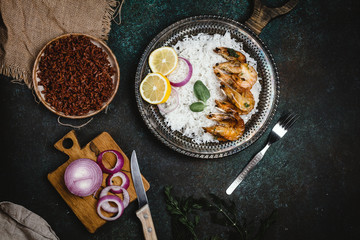 Top view of cooked shrimps with lemon and onion on rustic metal tray with rice side dish on dark table
